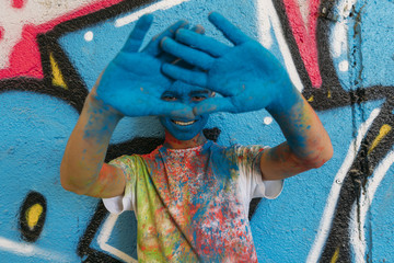 Teen smiling with hands in front of his face, is painted blue with a graffiti