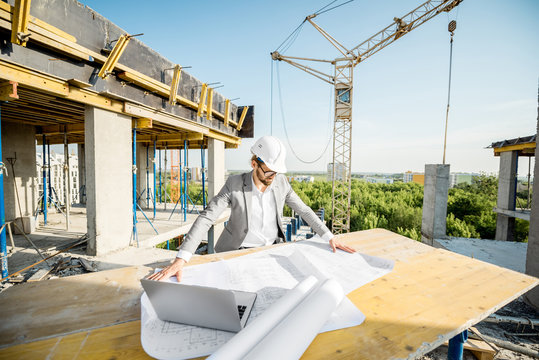 Handsome engineer working with architectural drawings at the table on the construction site outdoors