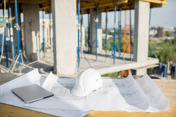 Workspace with architectural drawings laptop and protective helmet at the table on the construction...