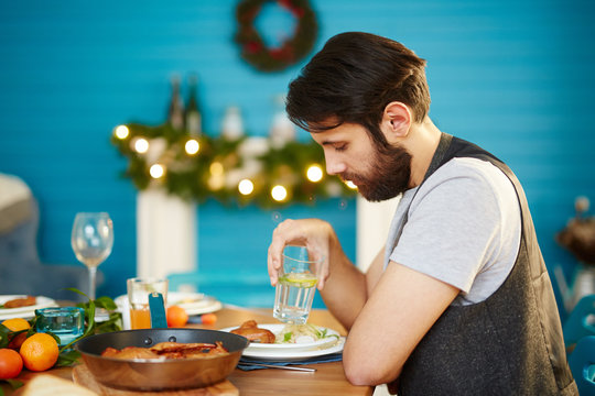Bored Attractive Male Sitting Alone At Table And Holding Glass During Dinner Party At Home