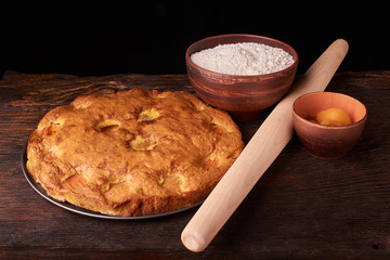 On a dark wooden table, fashionable bakeries, a bowl with flour, apricot cake and tools stand on table