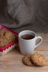 delicious oatmeal cookies with splash of sunflower seeds, sesame seeds on wooden table laid out in row on brown background with cup of tea