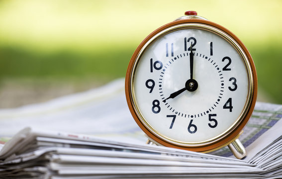 Time management concept - retro alarm clock on morning newspapers