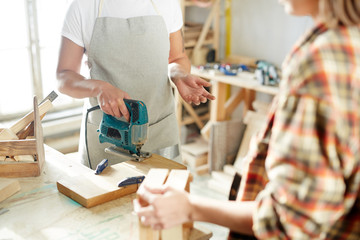 Two faceless woman standing near workbench in carpenter workshop and working with wood. 