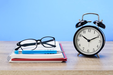 Concept Education or business : The glasses and blue pen placed on red book with black alarm clock...