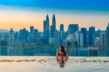 Asian travel and vacation. Young woman enjoying the city view from roof top swimming pool.