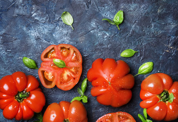 Red tomatoes with basil leaves on the black stone background, top view