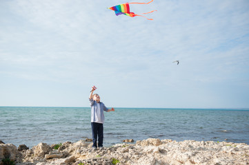 handsome little boy with flying kite on sea and sky background outdoors