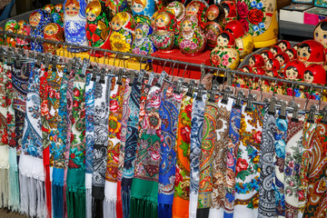 Many multicolored fabric scarves and painted dolls - matryoshkas, so-called Russian souvenirs, lie...