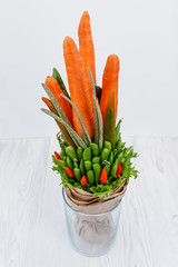 An original vegetable bouquet consisting of carrots, pea pods, lettuce leaves, red pepper and aloe is stand in a glass vase as a symbol of a healthy eating