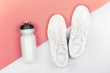Composition with sneakers and bottle of water on pink gray background, top view. Gym workout
