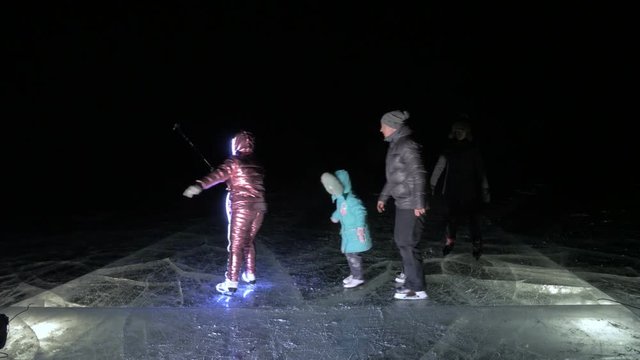 Family is ice skating night, make selfie. Mother, father, daughter and son riding together on ice in cracks. Outdoor winter fun for athlete nice winter weather. People on ice skates enjoying winter