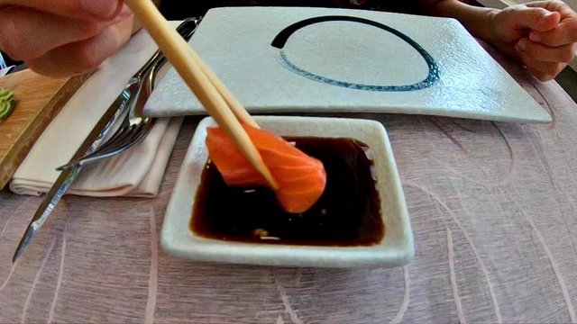 SLOW MOTION: hand feeding on salmon fillet in soy sauce bowl. Japanese fusion food, Asian cultures. Healthy food, light diet concept. Slow motion closeup feeding.