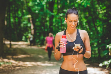 Sportswoman using smartphone app and walking on running track in the park.