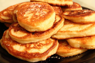 Pancakes sprinkled with sugar on a black plate. Pancakes with milk. Close-up.