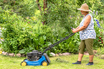 Woman gardener working in the garden, cutting grass with a mower. Lawn mowing in the summer garden.