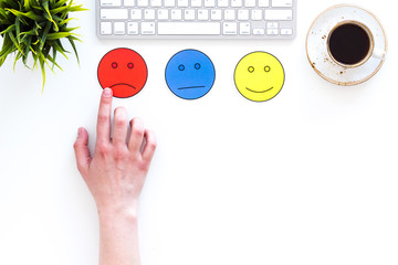 Evaluate customer service. Hand point emoji smiling, neutral, sad face on work desk on white background top view copy space