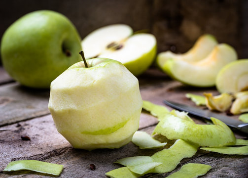 Green apple on wooden desk with knife and halved apples behind.