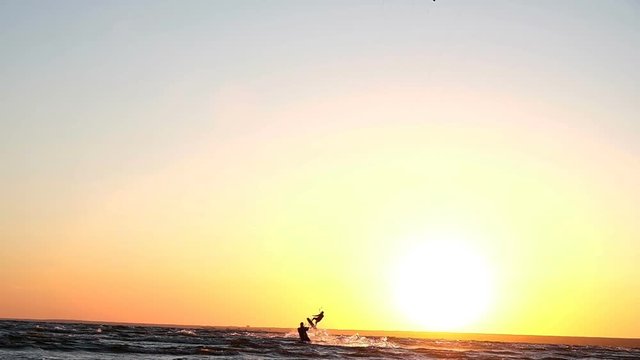 Kitesurfer does a trick in flight over the water against a sunset in summer, slow motion