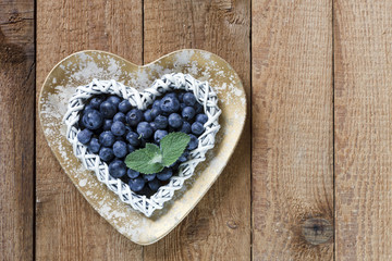 Fresh beautiful blueberries in shape of heart in plate on wooden table background. Top view