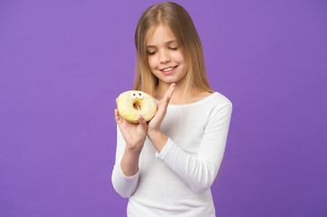 Girl on smiling face holds sweet donut in hand, violet background. Sweet tooth concept. Girl looking at donut with pair of eyes. Kid girl with long hair likes sweets and treats