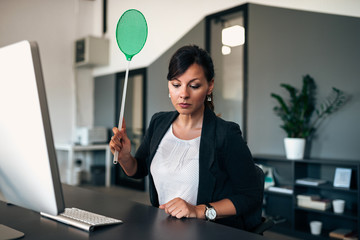 Serious business woman with flyswatter in the office.