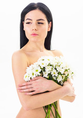 Girl on calm face naked holds chamomile flowers in front of breasts. Natural cosmetics concept. Woman with smooth healthy skin looks attractive. Lady covers breasts with flowers, isolated on white.