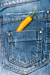 Hot sensations concept. Pepper in back pocket of blue jeans. Pocket of jeans staffed with yellow chilly pepper, denim background. Piquant secret in pocket of pants, top view