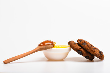 Cookies with chocolate drops and bowl with honey and wooden spoon, white background. Healthy sweets concept. Cookies and honey tasty sweets. High calorie food with honey, close up