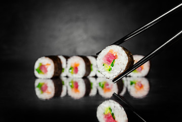 Chopsticks holding Sushi roll inari on black background made of Seaweed, marinated rice, cucumber,  Sushi menu. Japanese food. Free-space. Close-up.