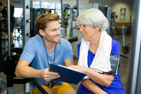 senior woman with male personal trainer exercising in gym
