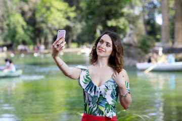 Girl take a selfie and smile. In the background the green lake in the outdoor park.