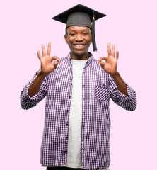 Young african graduate student black man doing ok sign gesture with both hands expressing...