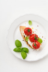 Sandwich with baked cherry tomatoes, garlic, olive oil and curd cheese on white background. Italian Cuisine. Top view.