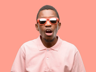 Obraz premium African black man wearing sunglasses scared in shock, expressing panic and fear