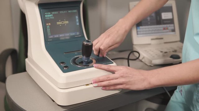 Close up shot of a doctor making adjustments on autorefractometer during patients visit. Medical staff. Machine for eyes checking.
