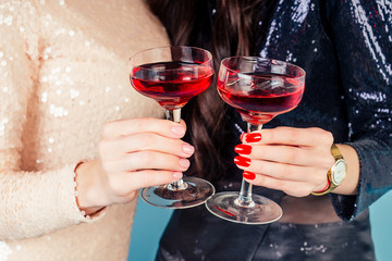 hands of two womens in evening cocktail shiny sequins dress are holding a glass of wine at a party in the studio blue background