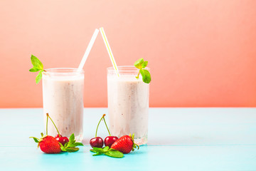 two glasses of smoothies made from milk, strawberries, banana, cherries, decorated with mint on bright pink blue background Concept healthy lifestyle, diet, tasty Copy space
