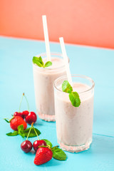 two glasses of smoothies made from milk, strawberries, banana, cherries, decorated with mint on bright pink blue background Concept healthy lifestyle, diet, tasty Copy space