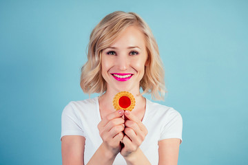 attractive and smiling woman blonde with make-up and lipstick on lips color fuchsia keeps a high-calorie cookie biscuit in hand in the studio on a blue background