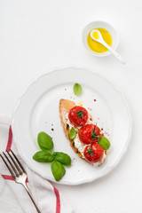 Sandwich with baked cherry tomatoes, garlic, olive oil and curd cheese on white background. Italian Cuisine. Top view.