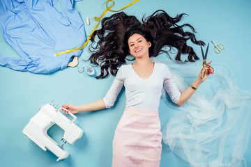 brunette woman seamstress tailor dressmaker lying (fly) on the floor with sewing machine, coats on...