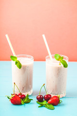Two glasses of milk smoothies with cherries, strawberries, banana and mint on bright background Concept of a healthy lifestyle. Place for copy space Tasty and healthy weight loss