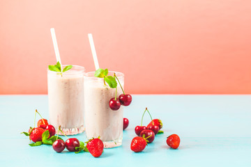 Two glasses of milk smoothies with cherries, strawberries, banana and mint on bright background Concept of a healthy lifestyle. Place for copy space Tasty and healthy weight loss