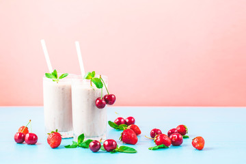 Two glasses of milk smoothies with cherries, strawberries, banana and mint on bright background Concept of a healthy lifestyle. Place for copy space Tasty and healthy weight loss