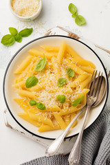 Penne rigate pasta with parmesan cheese and basil leaves in ceramic plate on gray vintage old concrete background. Selective focus.