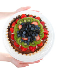 Young female hands holding a white porcelain plate with fresh summer fruit tart isolated on white background. Top view flat lay vertical presentation