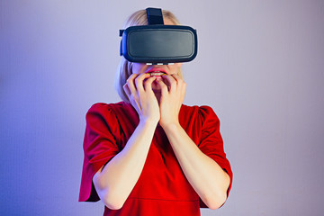 portrait of a young attractive amazed woman with blonde hair in the helmet (glasses) of virtual reality shocked and surprised