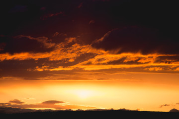orange clouds and golden sun beam at sunset horizon