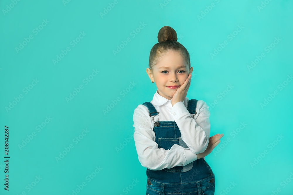 Wall mural beautiful little happy girl in jeans and a white shirt on a blue background